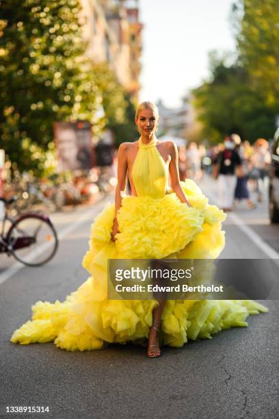 Leonie Hanne wears a yellow high-neck / backless / asymmetric ruffled large tulle dress with a long train co-created with Milla, gold pendant...