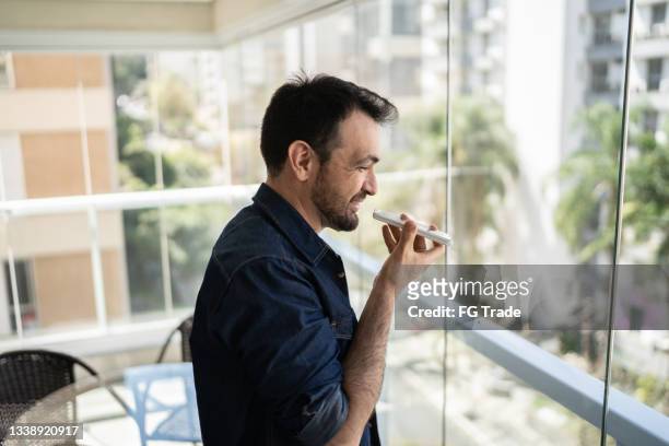 man sending audio message on smartphone from apartment's balcony - voice search stock pictures, royalty-free photos & images