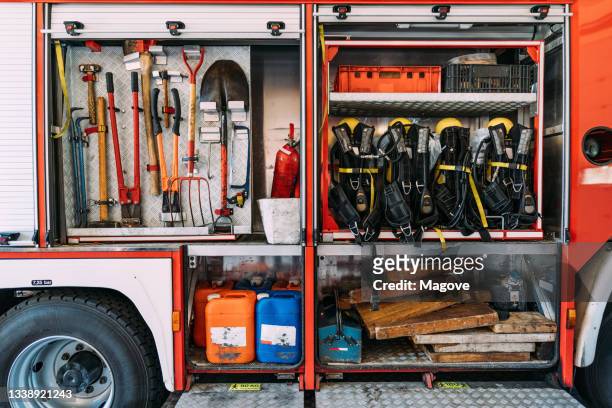 fire truck with plastic canisters under metal nippers and tire jack with fire extinguisher near similar safety vests in garage - quartel de bombeiros imagens e fotografias de stock