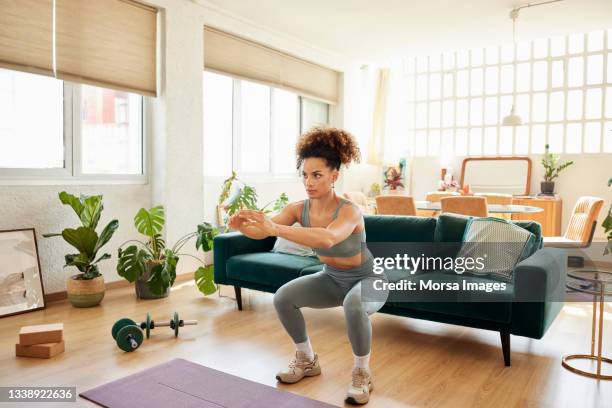young fit woman doing squats in living room - crouching stock pictures, royalty-free photos & images