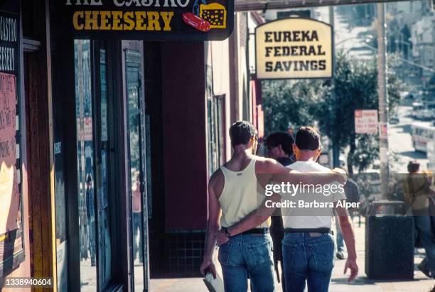 View, from behind, of two men as they walk, their arms one another, on a Castro Street sidewalk, San Francisco, California, November 1989.