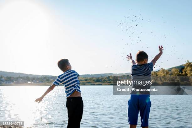 young boys having fun on the lake, throwing stones into the water. - throwing rocks stock pictures, royalty-free photos & images