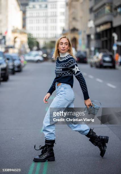 Sonia Lyson is seen wearing light blue jeans Weekday, Dior mini bag, Dior black laced boots, Dior knit with logo print during Fashion Week Berlin on...