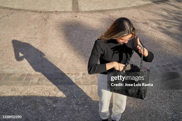 woman taking out the phone from the bag in the street. - handtasche stock-fotos und bilder