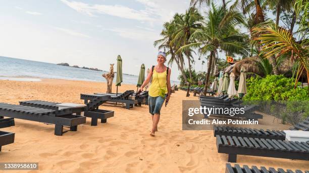 positive, happy european woman, a tourist, is walking on a tropical beach between unoccupied chaise-lounges - alex potemkin coronavirus stock pictures, royalty-free photos & images