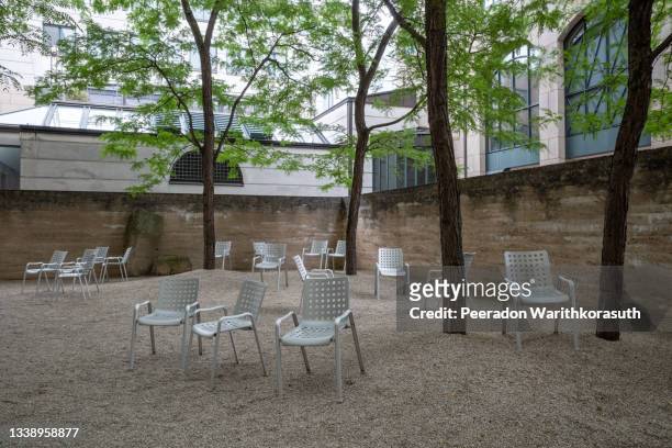 outdoor tranquil view of random chairs are spread on pebble ground of inner courtyard under shade of tree. - atrium architektonisches detail stock-fotos und bilder