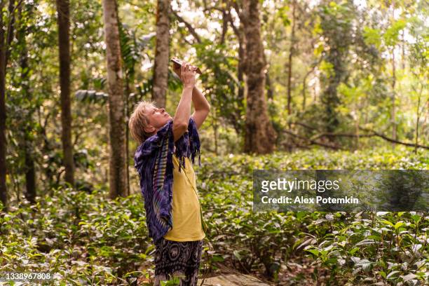 a 50-years-old positive caucasian white woman exploring tea plantation in sri lanka, taking pictures with her smartphone. - 50 54 years stockfoto's en -beelden