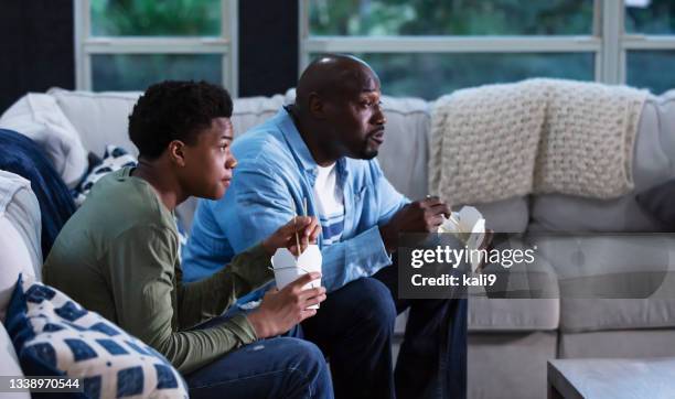 african-american father, son watch tv eating take out - boy jeans stockfoto's en -beelden