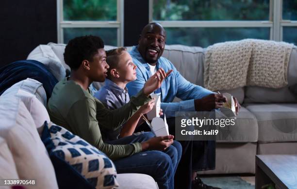 gemischte familie auf der couch, fernsehen, essen zum mitnehmen - child eat side stock-fotos und bilder