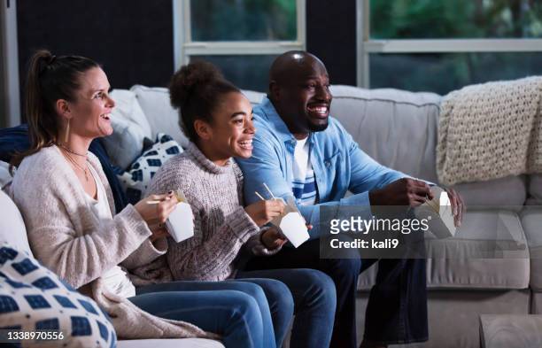 multi-ethnic family on couch watching tv, eating takeout - chinese takeout stock pictures, royalty-free photos & images