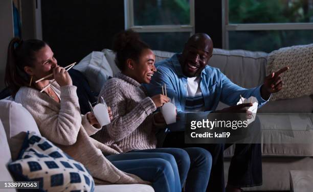 famille multiethnique sur le canapé en regardant la télévision, en mangeant des choses à emporter - child eat side photos et images de collection