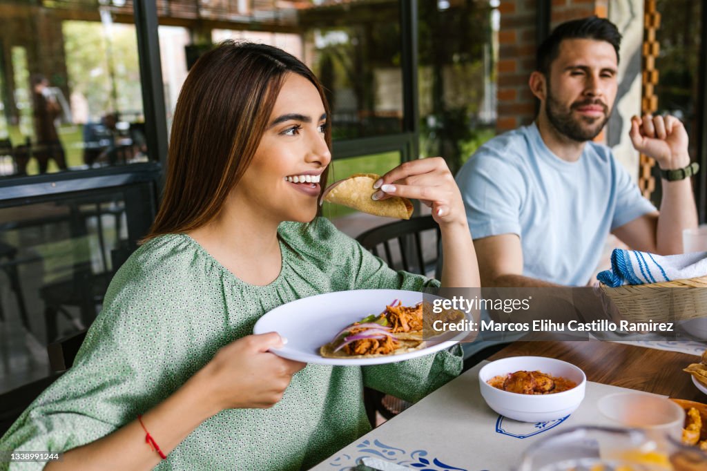 Young latin woman eating mexican tacos on a restaurant terrace in Mexico Latin America, feeling happy on a summer day