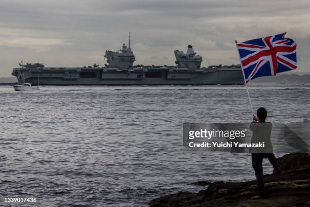 Man waves a British national flag as the British Royal Navy aircraft carrier HMS Queen Elizabeth sails out of Tokyo bay on September 08, 2021 in...
