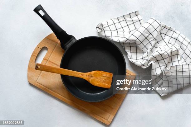 a new clean empty cast-iron frying pan and a wooden spatula, on a cutting board. the concept of cooking in a restaurant and cafe, at home in the kitchen. cook yourself, taking courses on the ability to cook delicious and beautiful food. - ustensile photos et images de collection