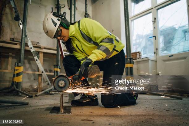 full length of female construction worker cutting metal while using electric saw at site - last day stockfoto's en -beelden