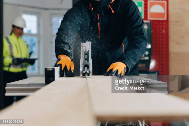 midsection of male worker using table saw for cutting wooden plank at construction site - table saw stock pictures, royalty-free photos & images