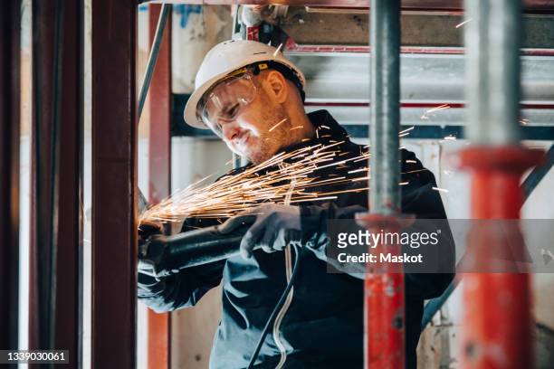 male construction worker cutting metal with machinery at site - protective workwear for manual worker stockfoto's en -beelden