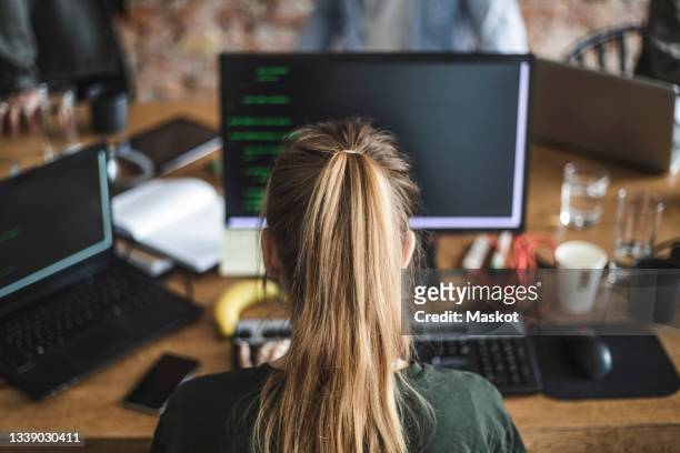 blond female programmer coding over computer in startup company - woman from behind foto e immagini stock