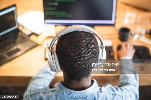 rear view of male hacker working on computer at office - black headphones stock pictures, royalty-free photos & images