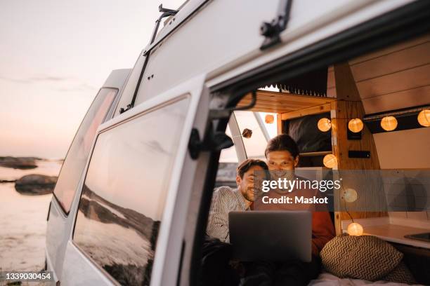 gay couple using laptop seen through doorway of camping van - campervan stock pictures, royalty-free photos & images