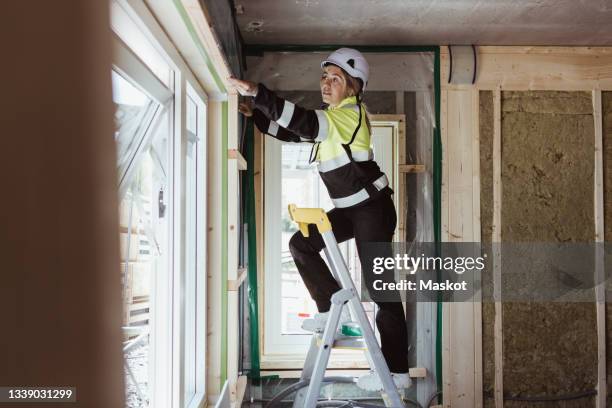full length of female building contractor measuring window frame standing on step ladder at construction site - step ladder stock pictures, royalty-free photos & images