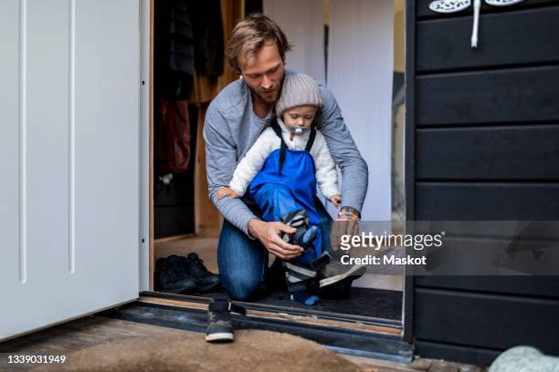 mid adult man helping son put on shoe at doorway - dresssing stock pictures, royalty-free photos & images