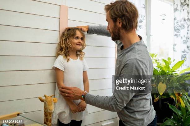 father measuring daughter's height at home - height stock pictures, royalty-free photos & images