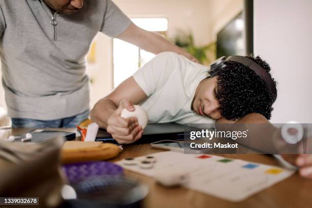 father looking at exhausted son resting over table at home - stress ball stock pictures, royalty-free photos & images