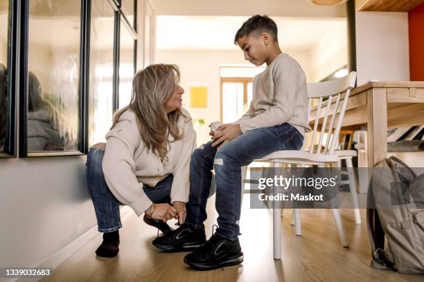 mother tying shoelace of autistic son sitting on chair in living room - mental disability ストックフォトと画像