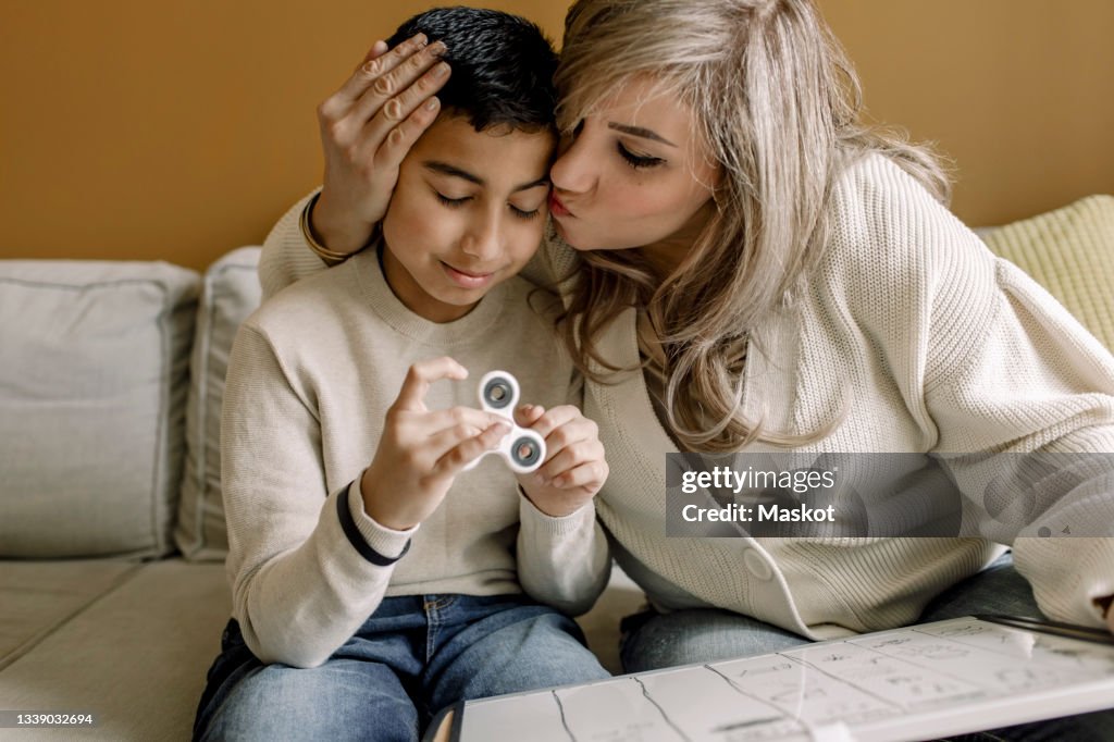 Mother kissing her son while they look over his homework together at home. He has ADHD and Autism and he uses a stim toy with his hands to help him focus.