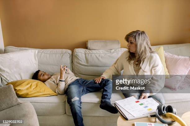 autistic son lying on sofa by mother in living room - math homework stock pictures, royalty-free photos & images