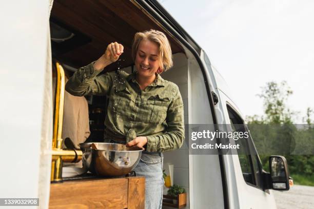 smiling girlfriend sprinkling salt while cooking in motor home - adicionar sal imagens e fotografias de stock