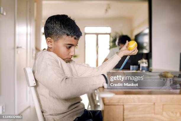boy learning while writing in book at home - stress ball stock pictures, royalty-free photos & images