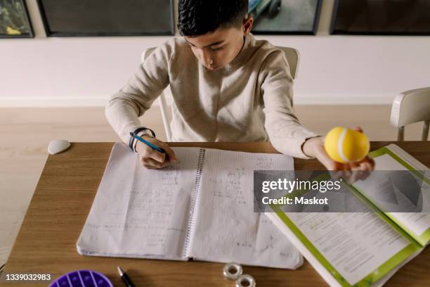 high angle view of boy writing in book at home - stress ball stock pictures, royalty-free photos & images