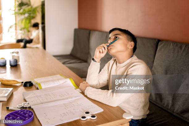 boy contemplating while sitting on sofa in living room - adhd stockfoto's en -beelden