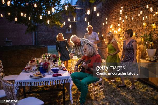 senior man playing acoustic guitar for his friends on garden party - senior man dancing on table stock pictures, royalty-free photos & images