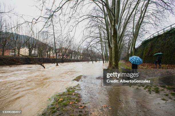 people walking along a flooded riverbank, olot, la garrotxa, girona, spain - sintflutartiger regen stock-fotos und bilder