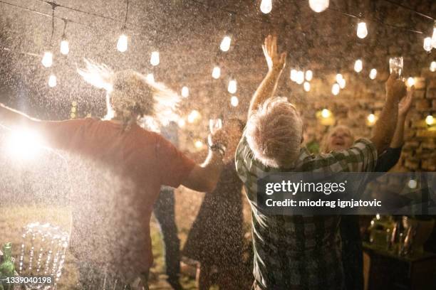 personas mayores bailando y disfrutando de la fiesta a pesar de la lluvia - champagne shower fotografías e imágenes de stock