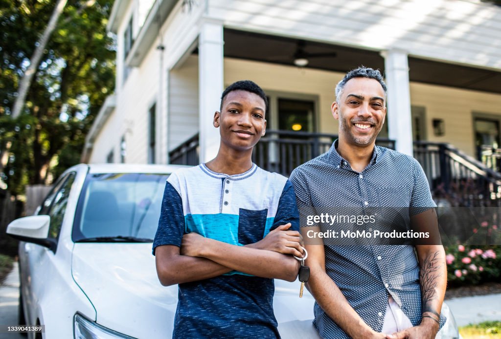 Portrait of young man and his father in front of his first car