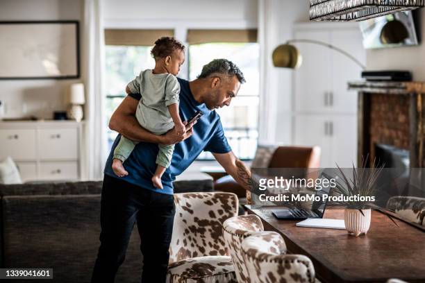man working from home while holding toddler - multitasking man stock pictures, royalty-free photos & images