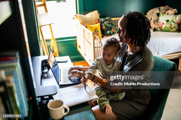 woman working from home while holding toddler - busy mom stock-fotos und bilder