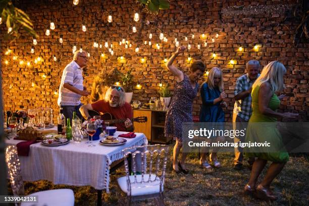 senior friends dancing and enjoying their time together on reunion party in backyard at night - senior man dancing on table stock pictures, royalty-free photos & images