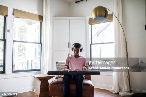 teenage boy with headphones playing keyboard at home - instrumento de tecla - fotografias e filmes do acervo