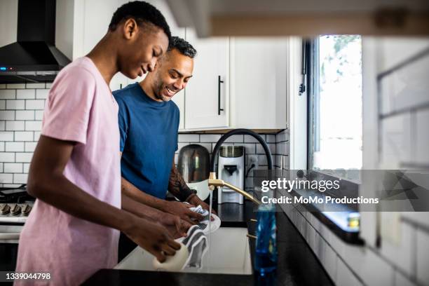 father and son washing dishes at home - haushaltsaufgabe stock-fotos und bilder