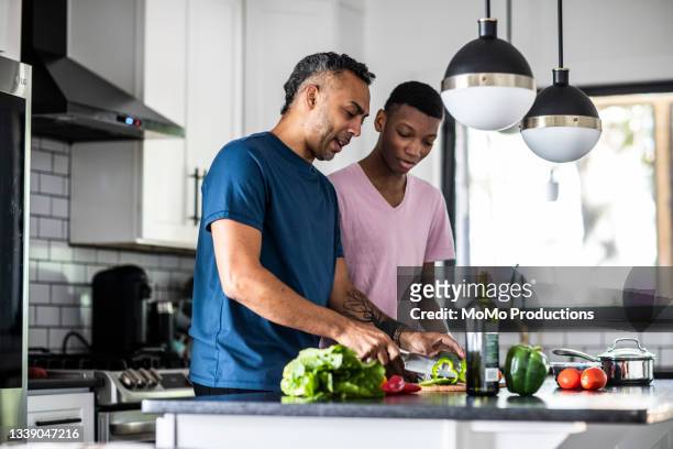 father and teenage son cooking together in kitchen - health food stockfoto's en -beelden