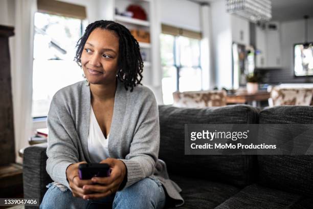 woman holding smartphone on sofa at home - woman relaxed portrait sitting stockfoto's en -beelden