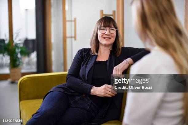 two businesswomen talking on couch in office - discussion stock-fotos und bilder