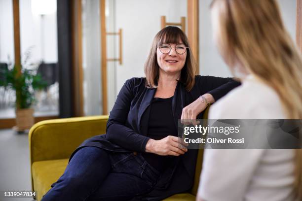 two businesswomen talking on couch in office - two men talking stockfoto's en -beelden