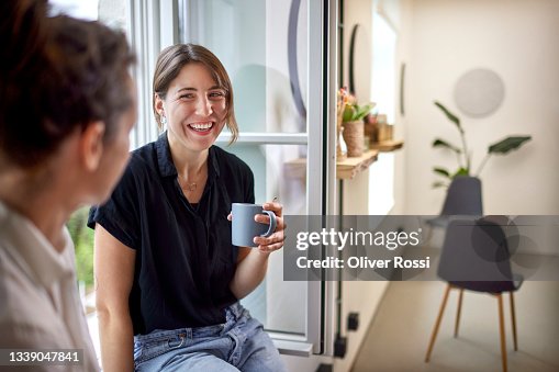 Two businesswomen having a coffee break at the window in office Two businesswomen having a coffee break at the window in office