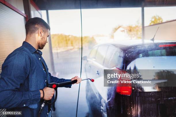 man washes the car with a hose before going on the road - valet stockfoto's en -beelden